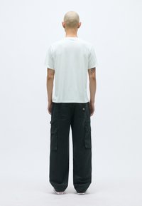 Bijela majica kratkih rukava i tamne cargo hlače s više džepova, prikazane sa stražnje strane na jednostavnoj svijetloj pozadini.