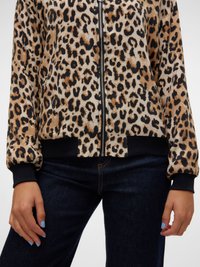 Veste bomber imprimée léopard avec un tissu doux, fermeture éclair à l'avant, poignets côtelés noirs et une ceinture contrastante. Associée à un jean foncé.