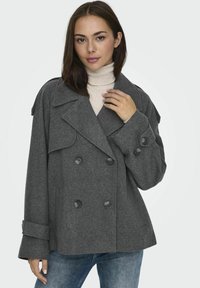 Péacoat en laine gris à double boutonnage avec de grands boutons noirs, col structuré et poignets retournés, porté sur un haut en col roulé de couleur claire.