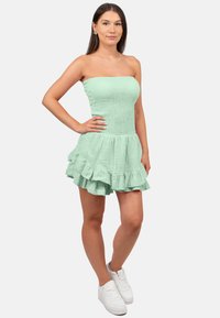 Mintgroene strapless jurk met een gestructureerde stof, een aangesloten lijfje en een gerimpelde zoom. Gecombineerd met witte sneakers.