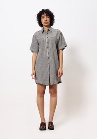 Hemdblusenkleid aus gestreiftem Stoff in Schwarz und Weiß. Mit kurzen Ärmeln, zwei vorderen Taschen und geradem Schnitt.