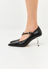 Décolleté in pelle nera con punta affilata, dotate di un cinturino con fibbia rotonda e tacco a spillo argentato metallizzato.