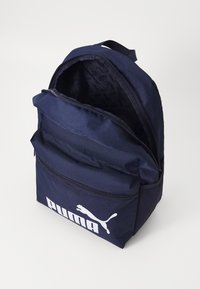 Marineblauwe rugzak van duurzaam materiaal met een groot hoofdvak en een voorvak met rits, voorzien van een opvallend wit logo. Gevoerde binnenzijde.