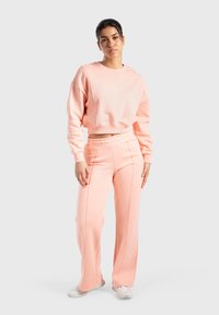 Lichtroze cropped sweatshirt en bijpassende wijde broek van zacht materiaal, met gestikte details en een elastische tailleband.