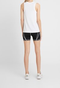 Biały bezrękawnik z okrągłym dekoltem, w połączeniu z czarnymi szortami sportowymi z białym kontrastowym szwem i dopasowanym krojem.