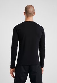 Svart långärmad t-shirt med rundad halsringning, mjuk textur och en diskret logotypdetalj på vänster ärm.