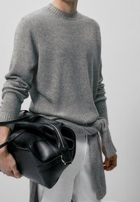 Grijze gebreide trui met geribde halslijn en manchetten, gecombineerd met een zwarte leren tas. De trui heeft een relaxed fit en lange mouwen.