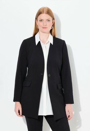 Černý blazer s jedním knoflíkem, dvěma předními kapsami, přiléhavý střih, nošený přes bílou košili s límečkem, minimalistický design, hladká textura.