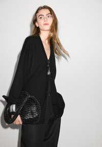 Svart cardigan med V-ringning, med knäppning framtill, överdimensionerade fickor och texturerade ärmar. Matchad med en vävd svart väska.