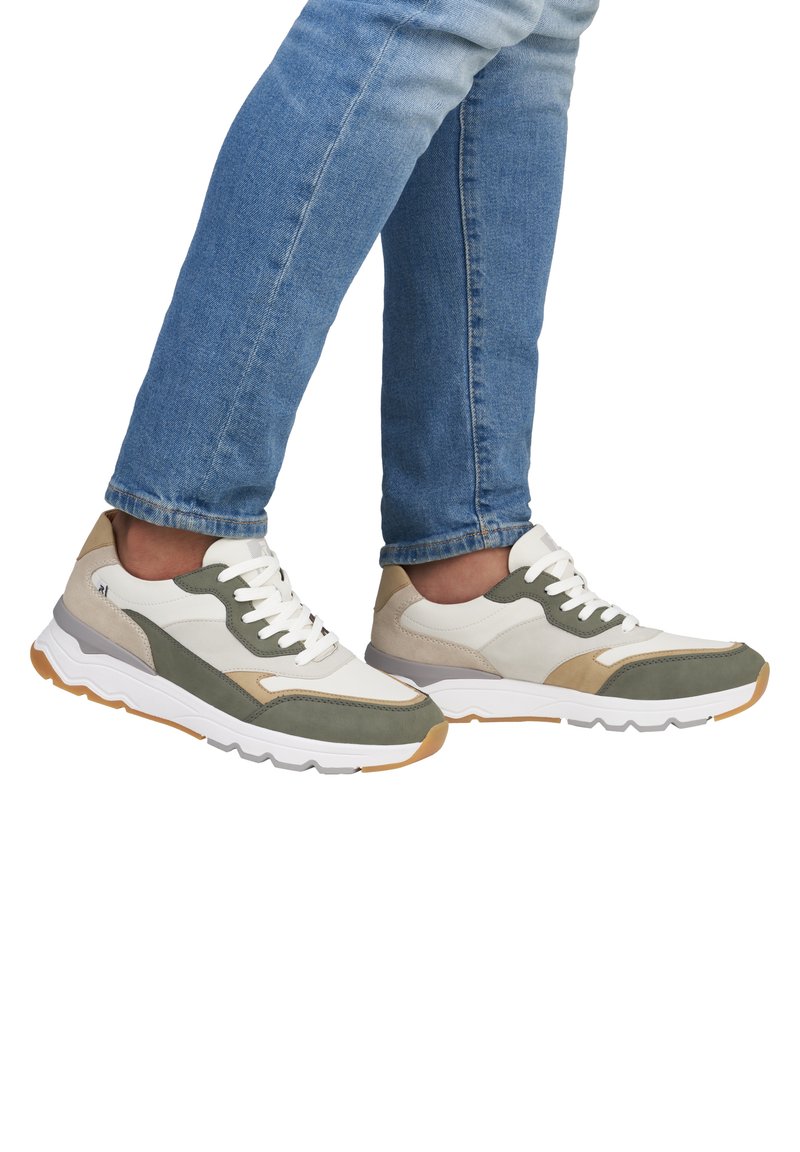 Les baskets présentent un mélange de daim et de textile crème, vert olive et taupe. Semelle blanche légère avec des accents texturés et de lacets épais.