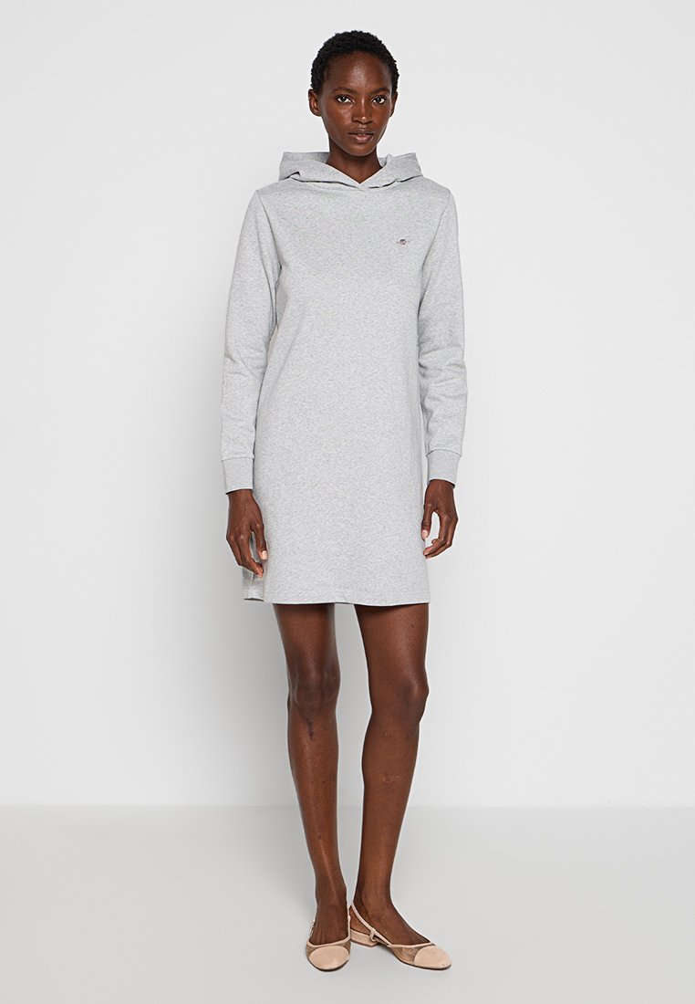 Vestido de sudadera gris de algodón con mangas largas, aberturas laterales y un bolsillo frontal. Diseño liso con un pequeño logo cerca del pecho.