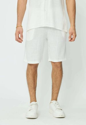 Shorts en lin blanc avec un motif texturé, dotés de deux poches avant et d'une coupe droite. Associés à des baskets blanches.
