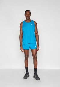 Μπλε αθλητικό τοπ χωρίς μανίκια και σορτς, με άνετη εφαρμογή και στρογγυλή λαιμόκοψη. Μαύρα αθλητικά παπούτσια με υφή και κάλτσες μέχρι τον αστράγαλο.