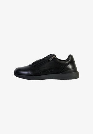 Zapatilla de piel negra con acabado suave, cordones, cremallera lateral y suela de goma. Presenta un diseño minimalista y un detalle de texto en el lateral.