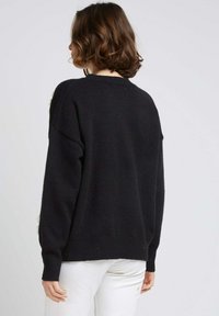 Pull en maille noir à coupe décontractée, à manches longues et avec un ourlet côtelé. Texture lisse ; la vue arrière ne présente aucun motif ou accent visible.