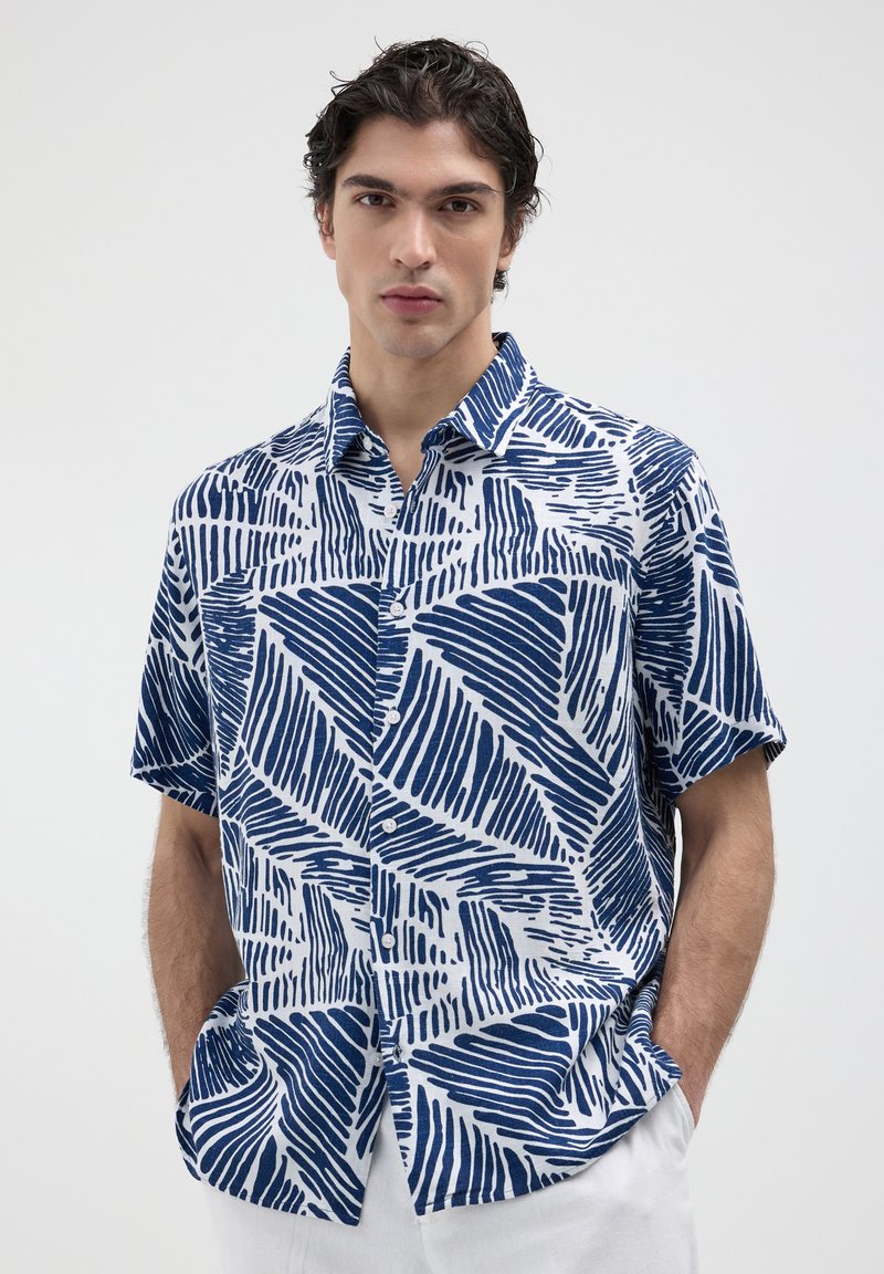 Camicia a maniche corte con bottoni bianca e blu, caratterizzata da un motivo geometrico a onde, colletto e vestibilità rilassata. Materiale in cotone.