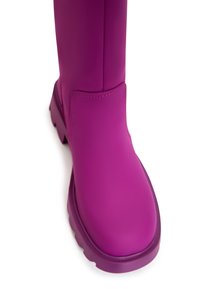 Fel paarse rubberlaars met een gladde matte afwerking, ronde neus en een stevige zool. Decoratieve stiksels langs de zijkant.
