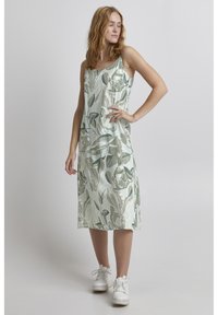 Vestido sin mangas con estampado floral en tonos verdes suaves, que presenta un corte holgado y una textura suave, combinado con zapatillas blancas.