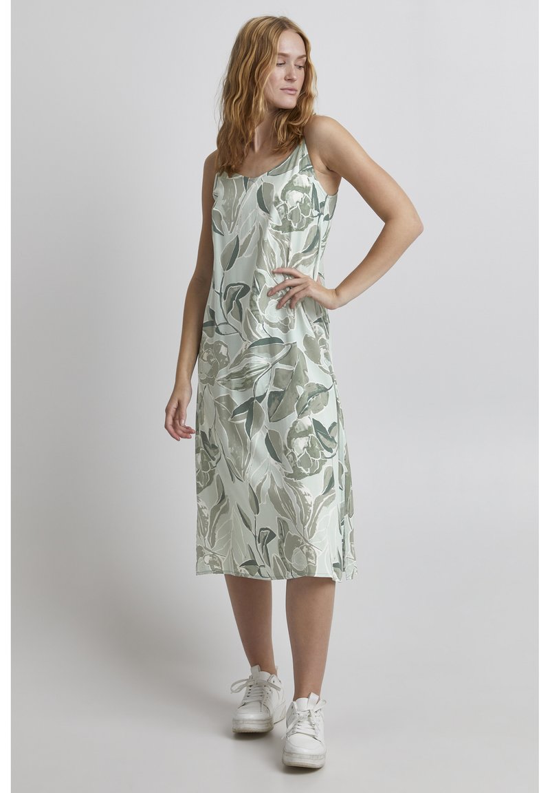 Vestido sin mangas con estampado floral en tonos verdes suaves, que presenta un corte holgado y una textura suave, combinado con zapatillas blancas.