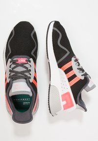 Black athletic shoes with mesh upper, pink and gray accents, textured sole, and three striped logo. Lightweight design for comfort.