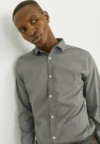 Chemise à motifs gris, à manches longues, avec un motif en losange et un col classique. Présente des boutons blancs et une texture de tissu lisse.