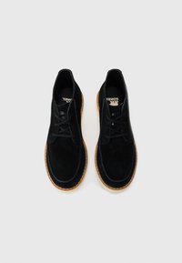 Black suede lace-up ankle boots with contrasting light brown soles viewed from above on a white background.
