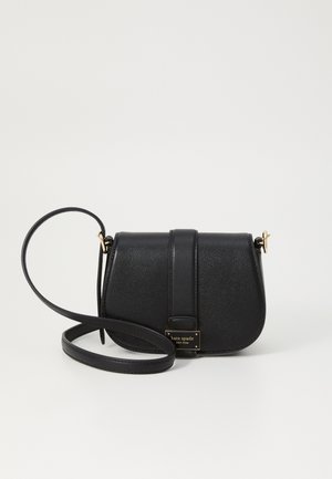 Černá kožená crossbody taška s klopou, zlatou destičkou "kate spade new york" a nastavitelným popruhem stočeným vpředu na bílém pozadí.
