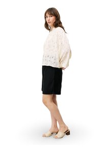 Lichtgewicht, crèmekleurig kanttop met bloemenpatroon, gecombineerd met zwarte shorts. Het model draagt beige muiltjes met een blokhak. Eenvoudig ontwerp in het algemeen.