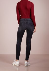 Jeans negros ajustados con cintura alta, diseño de cinco bolsillos y un ligero desgaste. Llevados con una camiseta roja de canalé y zapatillas blancas con detalles.