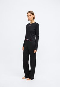 Camisa preta de manga longa com pequeno logótipo vermelho, combinada com calças largas pretas com cintura vermelha e preta. Textura suave e lisa.