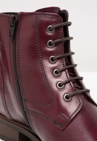 Burgundowe skórzane botki za kostkę o błyszczącej powierzchni, z metalowymi oczkami, szarymi sznurówkami, bocznym zamkiem błyskawicznym oraz kontrastowymi detalami szewnymi.