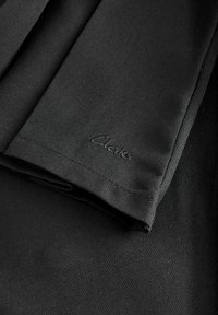 Tissu noir avec une finition texturée et un subtil éclat, comportant un logo brodé « Clarks » dans un coin. Design épuré et simple.