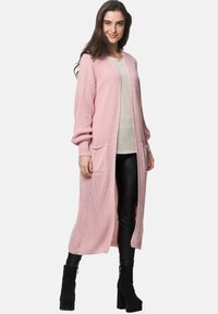 Lång, öppen cardigan i ljusrosa, med en strukturerad stickning, två framfickor och ribbad ärmknäppning, som är parat med en beige topp.