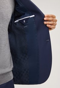 Navy Blazer Innenfutter mit einem gemusterten Futter und dezentem Glanz, einer Innentasche und einem Etikett mit der Aufschrift "EXTRA SLIM FIT". Glatte Textur.