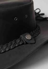 Black leather hat with a round crown, braided leather band, metallic accents, and ventilation grommets on the sides. Smooth texture.