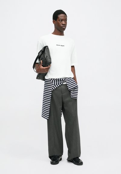 White short-sleeve t-shirt with "Maison" text, striped navy and white wrap, gray wide-leg trousers, black leather bag, and black shoes.