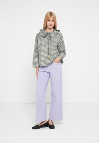 Blusa de cuadros vichy verde y blanca con cuello oversized, atada en el cuello; combinada con pantalones lila de pierna ancha y textura, y zapatos planos negros.