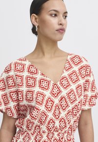 Abito a righe rosse e crema con scollo a V e maniche corte, caratterizzato da un design geometrico e dettaglio in vita arricciato.