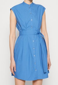 Blauwe katoenen overhemdjurk met een mandarijnkraag, korte kapmouwen, knoopsluiting aan de voorkant en een ceintuur in de taille. Gladde textuur en knie- lengt.