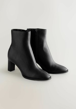 Schwarze Lederstiefeletten haben eine spitze Zehenpartie und einen Blockabsatz. Das Design umfasst einen seitlichen Reißverschluss für ein einfaches An- und Ausziehen. Glatte Textur über die gesamte Stiefelette.