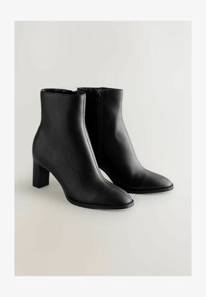 Zwarte leren enkelboots hebben een spitse neus en een blokhak. Het ontwerp bevat een zijrits voor gemakkelijke aan- en uittrekken. Gladde textuur overal.