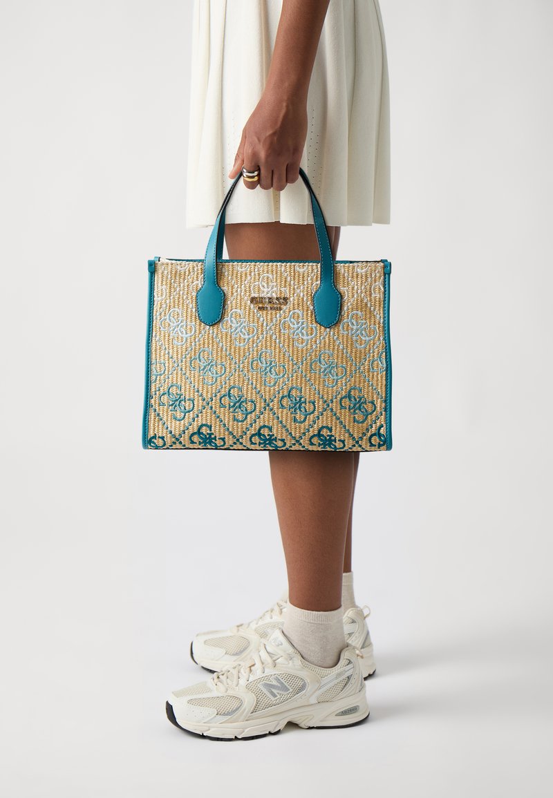 Woven straw tote bag with turquoise leather handles, featuring a geometric pattern, logo detail, and a rectangular shape.