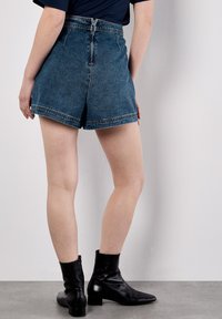 Dunkelblaue, hochgeschnittene Denim-Shorts mit aufgerollten Säumen und einem Reißverschluss. Kombiniert mit schwarzen Knöchelstiefeln.