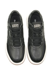 Schwarze Sneakers aus Leder und Mesh, mit runden Perforationen, strukturierten Akzenten und weißen Gummisohlen. Markenlogo auf der Zunge sichtbar.