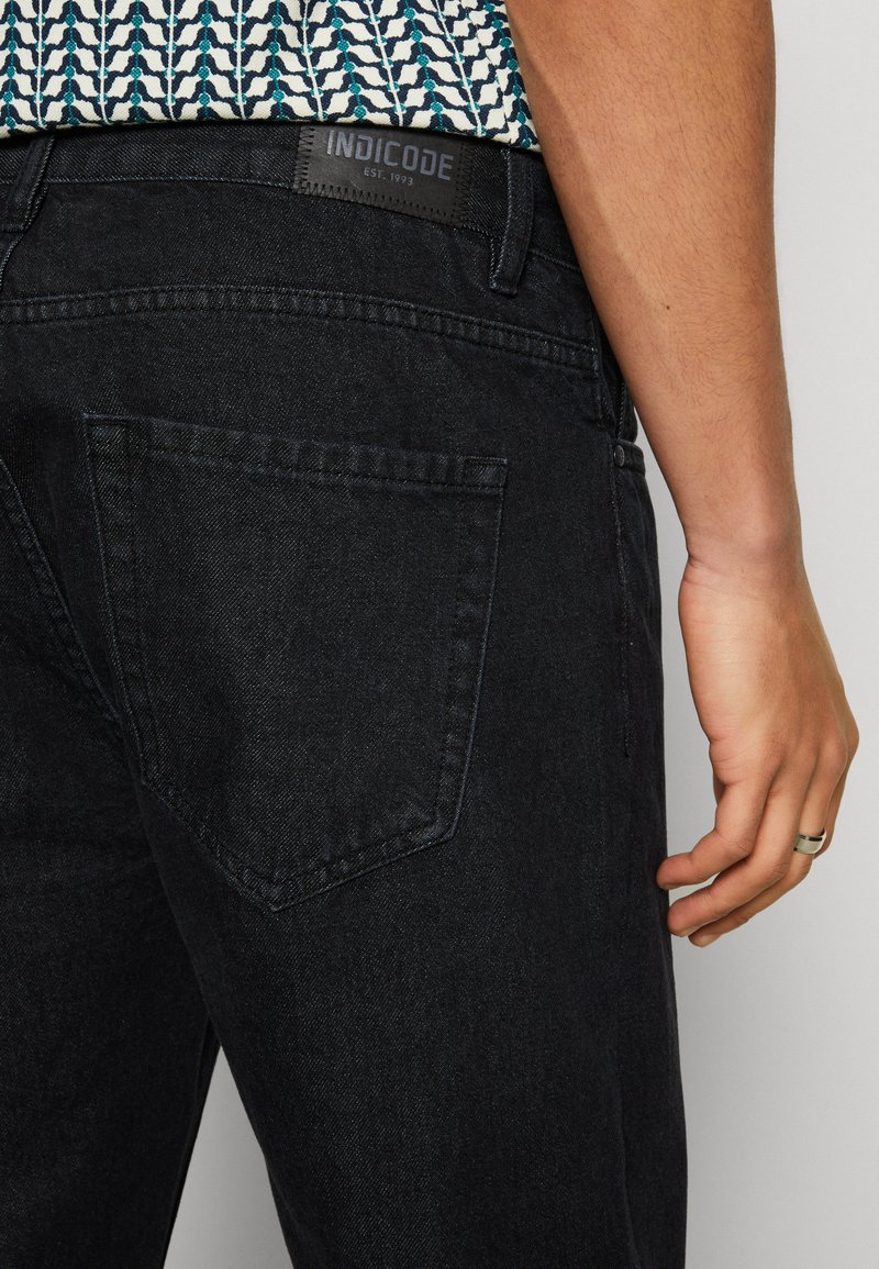 Schwarze Denim-Jeans mit geradem Schnitt, ausgestattet mit einer Gesäßtasche und einem sichtbaren Markenlabel. Glatte Textur und minimalistisches Design.