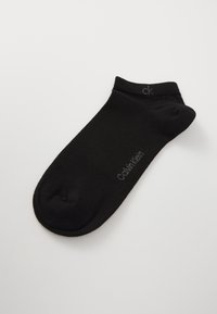 Schwarze Knöchelsocke aus gestricktem Material, mit glatter Textur und einem Logo, das in Grau auf der Seite "Calvin Klein" liest.