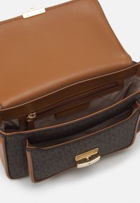 Wnętrze torby z brązowej skóry i wzorzystej tkaniny z kieszenią na zamek, dwoma przegródkami oraz złotym zapięciem.