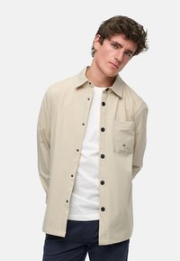 Beige knapp-up skjorte laget av lett stoff, med brystlomme, svarte knapper og et rent, minimalistisk design.