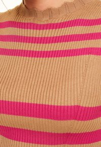 Haut en maille côtelée beige avec larges rayures roses. Il présente un col festonné et un détail poche sur le devant à gauche.
