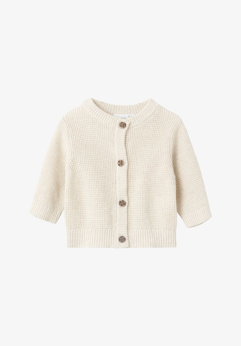 Κρεμ κασκόλ πλεκτό με στρογγυλή λαιμόκοψη, κοντά μανίκια και ξύινες κουμπότρυπες μπροστά. Υφασμάτινο σχέδιο σε όλη την επιφάνεια.